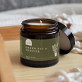 Candle jar labeled 'Green Fig & Vetiver' on a wooden surface with soft lighting.
