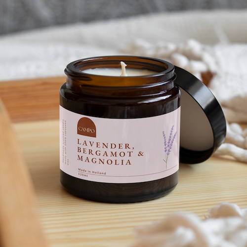 Candle jar labeled 'Lavender, Bergamot & Magnolia' on a wooden surface with soft lighting.